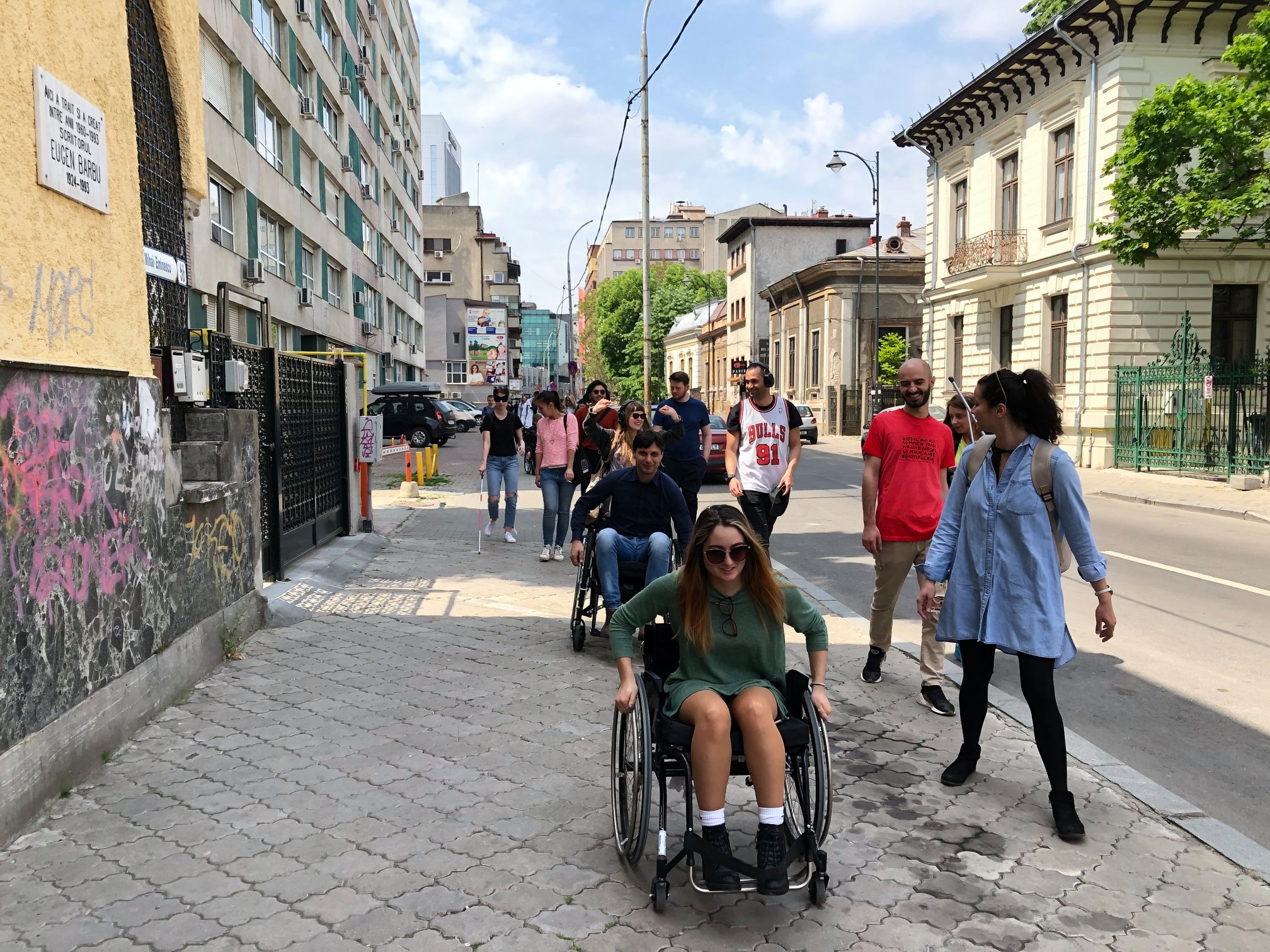 Students are walking on a narrow street using opaque glasses, canes and wheelchairs.