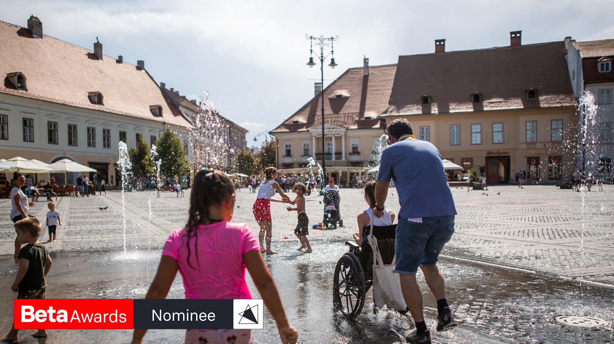 the main photo with diverse people playing in a water fountain with the label nominee on it